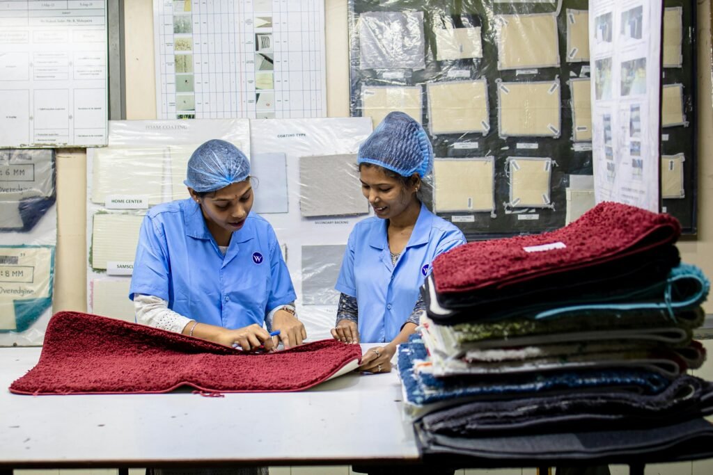 Present. Precise. Accountable. Two women in a textile factory inspecting red fabric samples in an industrial setting.